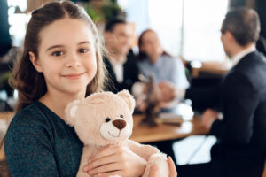 A girl hugs a teddy bear while her parents talk to a family law lawyer in Waleska.